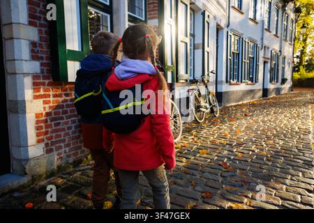 Two children with backpacks walking along cobblestone street Stock Photo