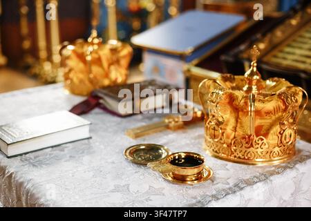 Ornate golden crowns for Orthodox wedding ceremony and a holy religious book on a table. Traditional Christian marriage sacrament, church altar setup Stock Photo