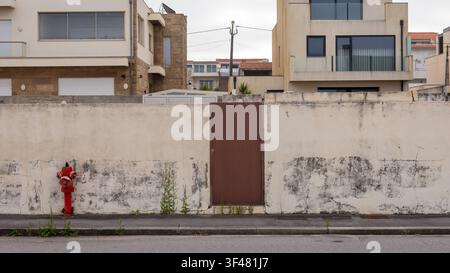 Red fire hydrant and rusted steel door in a weathered concrete wall on a suburban street, Portugal Stock Photo