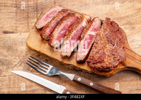Grilled beef ribeye steak sliced medium rare on wooden board with knife and fork. Stock Photo