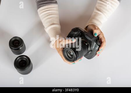 Holding DSLR Camera with Zoom Lens and Additional Lenses on White Surface Stock Photo