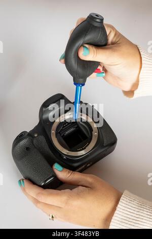 Vertical close-up of cleaning a DSLR camera sensor with an air blower Stock Photo