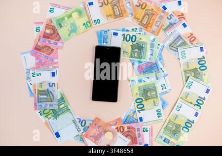 Black smartphone with a whirlwind of euro banknotes flying out on a pink background, symbolizing constant online spending and digital cashflow. Stock Photo