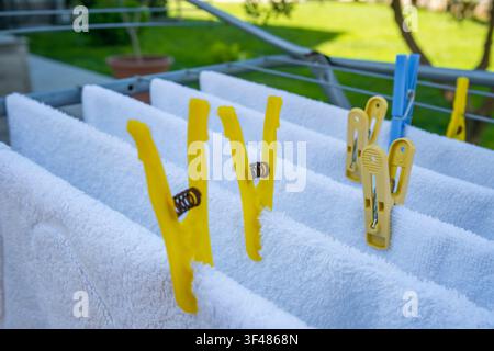 Clothes drying on a rack outdoors. White towels are clipped with colorful clothespins. Green grass and trees are visible in the background. Stock Photo