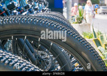 Close-up of black bicycle wheels lined up in row showing textured tread surface with blurred pedestrians in urban outdoor background. Stock Photo