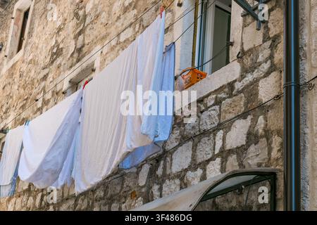 Clothes hanging on line outside light-colored stone building in bright sunny Mediterranean setting showcasing everyday domestic life. Stock Photo