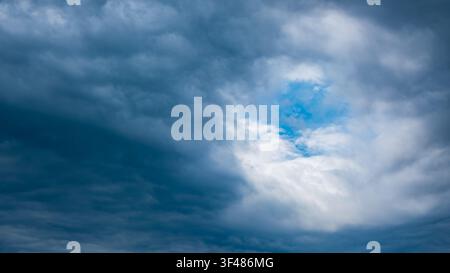 Dramatic sky with dark clouds and a small patch of blue. The clouds are thick and layered, creating a moody atmosphere. Stock Photo