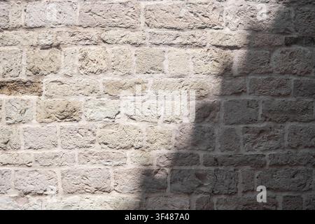 A textured stone wall with a light shadow cast on it. The stones are light-colored and irregularly shaped, creating a rustic appearance. Stock Photo