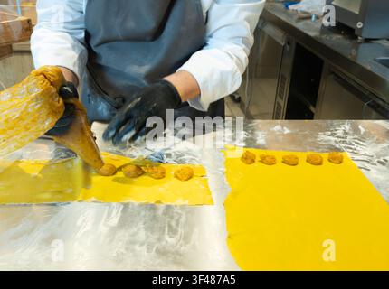 Chef's hands stuffing fresh cappelletti pasta with filling on a stainless steel counter Stock Photo