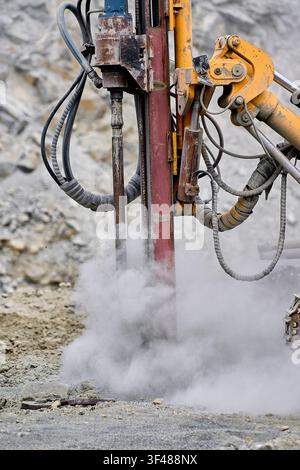 A powerful drilling machine operates in an open-pit copper mine, surrounded by dust and rock debris, showcasing the industrial process of copper extra Stock Photo