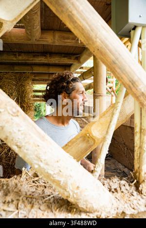 A builder stands inside a sustainable bamboo structure during the construction process. The image conveys craftsmanship, natural materials and the pro Stock Photo
