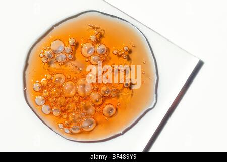 Close-up of orange vitamin C facial serum oil drops with cosmetic bubbles on a clear glass plate, clean skincare background for beauty, spa, and cosme Stock Photo