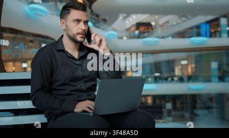 Serious Caucasian businessman working laptop talking mobile phone in business center man male guy work with computer talk smartphone focused employer Stock Photo