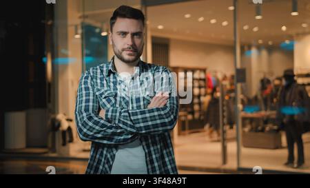 Confident serious calm Caucasian client buyer man crossed hands posing in shopping mall customer male guy crossing arms feeling confidence near shop Stock Photo