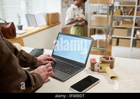 Adult Man Updating Order Data on Laptop for Small Business Shipping Stock Photo