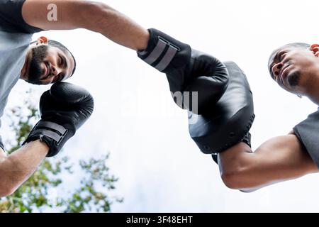 Two friends practice boxing outdoors, exchanging intense punches with focus and energy. The image captures the dynamic scene from a low-angle perspect Stock Photo