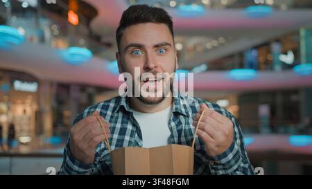 Portrait happy excited smiling Caucasian man opening shopping bag look inside satisfied with goods purchases amazed male buyer customer open package Stock Photo