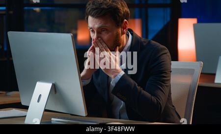 Upset Caucasian 40s business man with headache computer overtime work in office late night tired middle-aged businessman mature male manager working Stock Photo