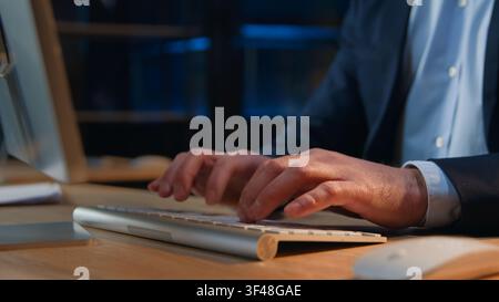 Close-up male hands typing computer keyboard in dark late office at night evening unrecognizable Caucasian business man male businessman working Stock Photo