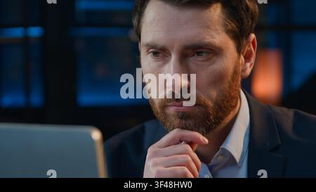 Close up puzzled pensive thinking Caucasian business man thinking looking at screen at night dark late evening office thoughtful businessman middle Stock Photo