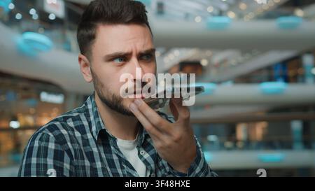 Caucasian serious worried male man recording voice mail with mobile phone app in shopping mall frown guy record audio message with easy smartphone Stock Photo