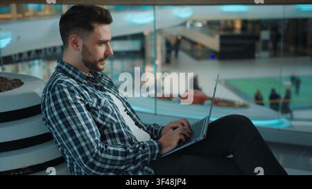 Gadget addicted Caucasian man freelancer student male working with laptop distant in business center focused male guy work studying with computer e Stock Photo