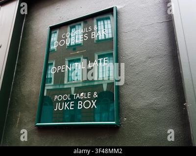 Outdoor pub sign in Manchester UK reflecting a building facade and promoting cocktails, pool table and juke box. Stock Photo