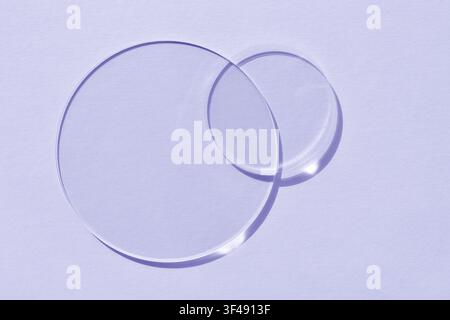 Transparent glass cosmetic discs casting soft shadow on pastel lavender background. Minimal abstract beauty and skincare concept. Top view with space Stock Photo