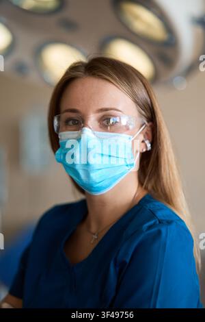 Portrait of vascular surgeon adjusts protective glasses in modern surgical room. Phlebologist wears medical mask and sterile gloves for operation. Stock Photo