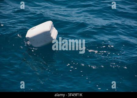 A discarded white plastic container floating as marine pollution on the blue ocean surface waves. Stock Photo