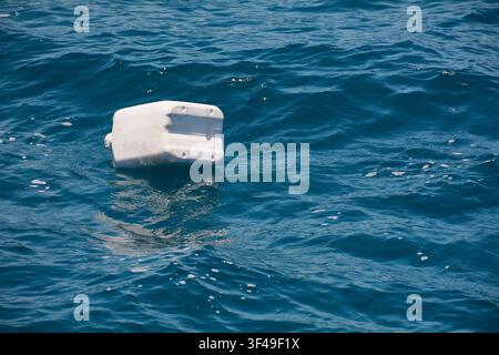 A white plastic container floats on the blue surface of the sea, highlighting issues of marine pollution and plastic waste. Stock Photo