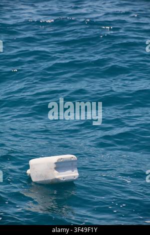A white plastic jug floats on the blue open ocean, representing environmental issues of marine pollution and litter. Stock Photo