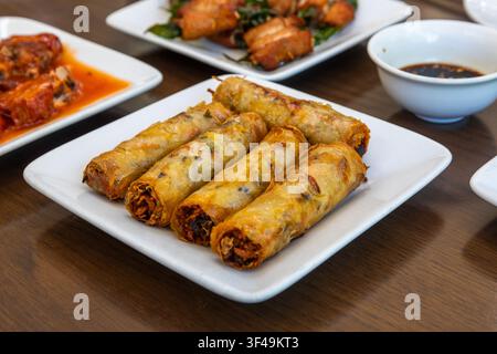 Crispy Vietnamese ch gio - fried spring rolls - serving on a white plate with dipping sauce and other dishes in background Stock Photo