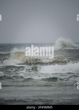 Powerful breaking ocean waves with sea spray under an overcast coastal sky. Stock Photo