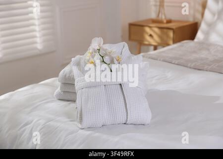 Clean bathrobe with flowers and towels on bed indoors Stock Photo
