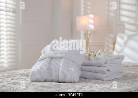 Clean bathrobe, towels and flowers on bed indoors Stock Photo