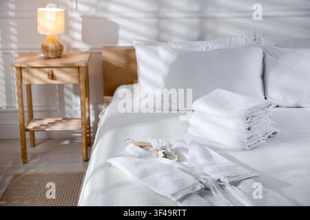 Clean bathrobe, towels and flowers on bed indoors Stock Photo