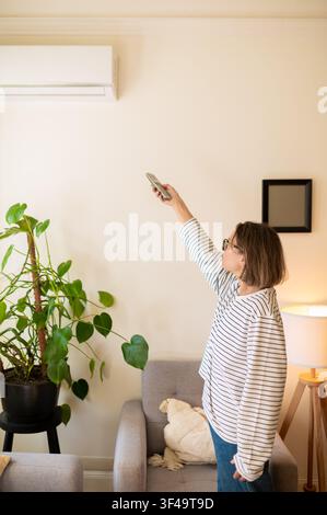 Middle aged woman using air conditioner remote control Stock Photo