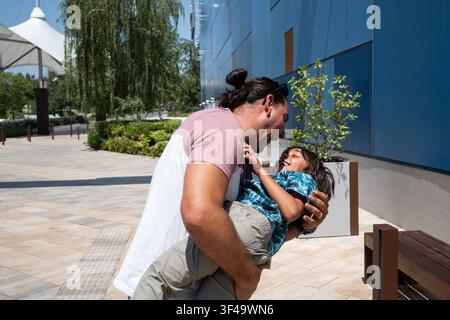 Happy father holding and playing with his laughing son outside Stock Photo
