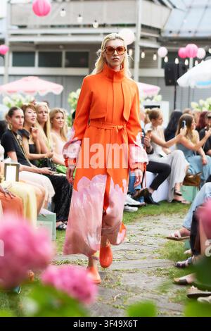 Munich, Germany, 16th Jul, 2026. Model walks the Marcel Ostertag SS27 Dancing Flowers runway in an orange belted coat with pink floral prints. Stock Photo