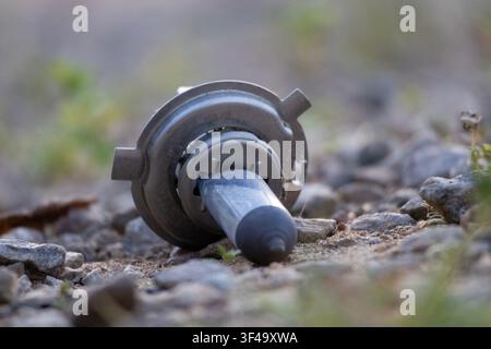 Car headlight bulb lying on the ground among gravel pebbles and a green smooth background and foreground Stock Photo