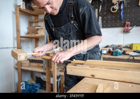Man carpenter working at workbench with instruments and old wooden board in restoration workshop. Stock Photo