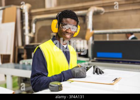 Worker wearing safety gear checking documents at lumberyard Stock Photo