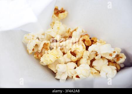 Fresh popcorn in a white paper bag, popular sweet snack food at events and in movie theaters, copy space, selected focus, narrow depth of field Stock Photo