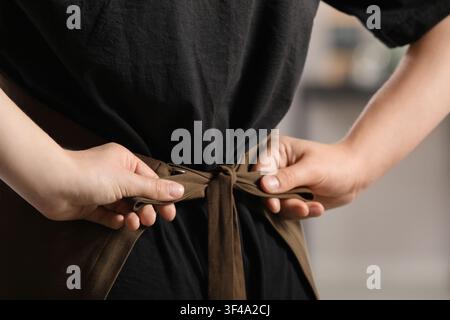 Person tying a brown apron around their waist, preparing for work in a professional setting, the hands are focused on creating a knot with the apron s Stock Photo