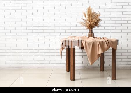 Wooden table with a beige tablecloth and dried pampas grass in a vase against a white brick wall, the setting is against a textured white brick wall, Stock Photo