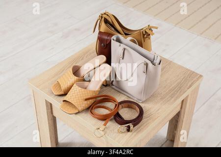 Stylish womens fashion accessories including woven mules, leather handbags, and belts on a light wooden table Stock Photo