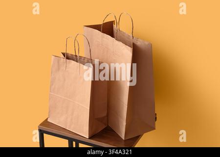 Two brown paper shopping bags with handles on a wooden table against a solid orange background retail and consumerism, the bags are of different sizes Stock Photo