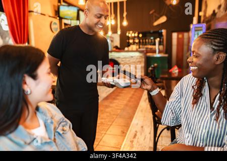 Woman paying with smartphone through terminal, waiter serving Stock Photo