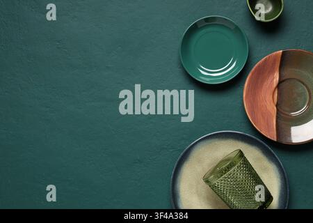 Empty green and brown ceramic plates with a textured glass on a dark teal background, top view with copy space, the composition features various dinne Stock Photo
